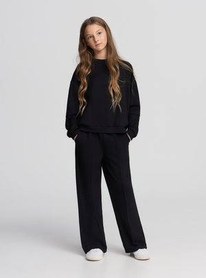 Felpa nera e pantaloni abbinati realizzati in materiale morbido. La felpa ha un collo tondo e una vestibilità ampia, mentre i pantaloni presentano una silhouette rilassata.