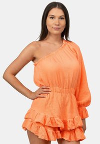 Eén-schouder oranje romper van textuurstof, met een elastische tailleband en gelaagde rucheshorts aan de onderzijde.