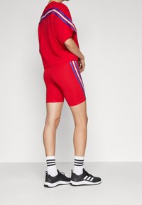 Une personne portant un short de sport rouge et un haut à rayures bleu et blanc, des chaussettes blanches avec des rayures noires et des baskets noires Adidas.