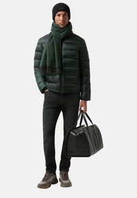 Zelená prošívaná bunda, černá čepice a šála. Tmavé džíny, šedé a hnědé tenisky. Drží černou koženou kabelu.