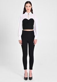 Top corto nero con scollatura a cuore e maniche lunghe bianche; abbinato a pantaloni neri a vita alta e tacchi neri.