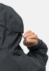 Zwarte waterdichte jas met een gestructureerde capuchon en trekkoord. Een hand past het trekkoord aan, wat de subtiele textuur van de stof onthult.