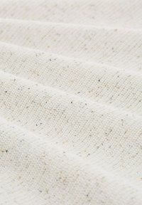 Weißer, strukturierter Stoff mit einem gewebten Muster, der kleine Farbkleckse aufweist und eine leicht unregelmäßige Oberfläche schafft.