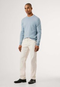Maglione lavorato a maglia azzurrino, jeans bianchi e stivali neri alla caviglia. Il maglione ha polsini a coste, i jeans sono a taglio dritto con cuciture visibili.