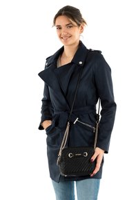 Cappotto trench navy con vita regolabile, colletto ampio e bottoni argento. Abbinato a una borsa a tracolla nera intrecciata con dettagli dorati.