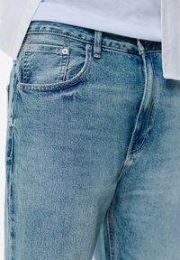 Jeans din denim albastru deschis cu un croi clasic. Dispune de cinci buzunare, cusături vizibile și o ușoară decolorare pentru un efect purtat.