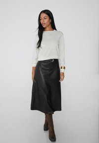 Falda midi de cuero negra con una silueta recta, que presenta una costura frontal y un cinturón con hebilla plateada. Combinada con un top de punto de color claro.