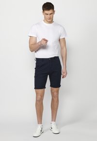Shorts en coton bleu marine avec un ourlet roulé, dotés de poches avant et d'une passant de ceinture, associés à un t-shirt blanc uni et des baskets blanches.