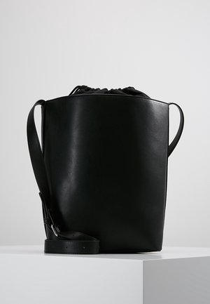 Musta nahkainen ämpärilaukku, jossa on nyörikiinnitys, minimalistinen muotoilu, sivukahvat ja irrotettava hihna. Tasainen pinta, ei kuvioita.
