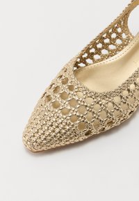 Chaussure à talon slingback dorée et texturée, avec un bout pointu et un design ouvert et tissé, dotée d'une doublure intérieure lisse et de quelques accents matériels discrets.