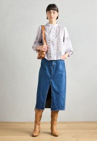 Gaiši violeta blūze ar mežģīņu detaļām, kombinēta ar džinsu maksi svārkiem ar priekšējo šķēlumu. Izskatu papildina brūna ādas plecu soma un zābaki.