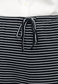 Pantalon rayé horizontal noir et blanc avec une ceinture à cordon nouée, associé à une chemise blanche côtelée boutonnée.