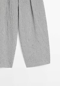 Vue recadrée d’un pantalon large à rayures verticales noires et blanches, posé à plat sur un fond blanc.
