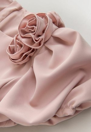 Tela rosa con detalle de volante floral fruncido en un textil suave y fluido, destacando la textura y las costuras.