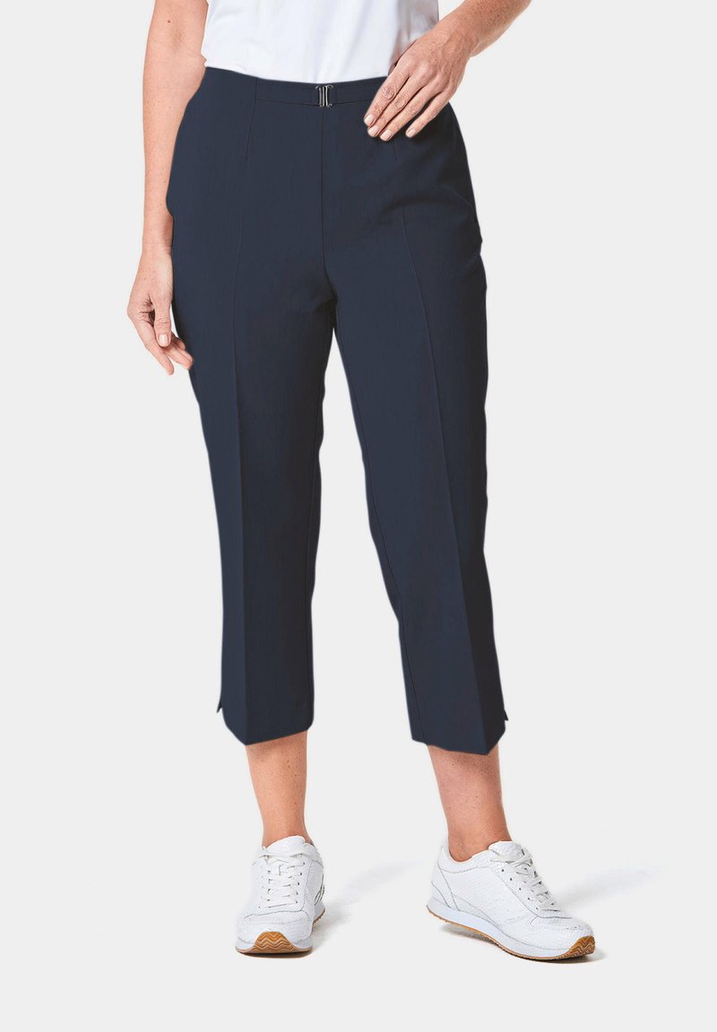 Pantalons cropped bleu marine avec une texture lisse, dotés d'une fermeture à glissière à l'avant et de deux poches inclinées. Associés à des baskets blanches.