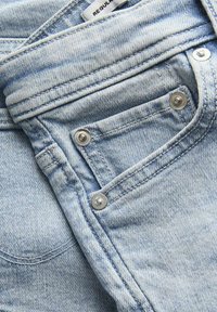 I jeans in denim blu chiaro presentano un design tradizionale con una piccola tasca frontale, rivetti metallici e dettagli di cucitura sottili.