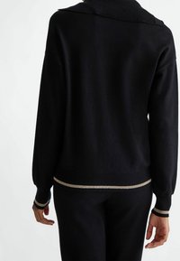 Czarny sweter z prążkowanym kołnierzem i mankietami, z złotym paskiem dekoracyjnym na dole. Miękka tekstura i luźny krój.