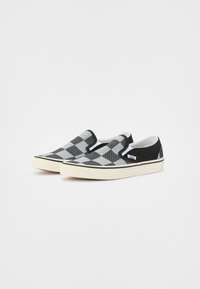 Zapatillas de lona a rayas negras y grises, tipo slip-on, con una parte superior de lona, forro suave y suela de goma crema. Presentan un detalle negro en el talón.