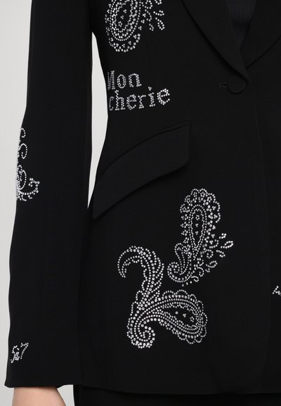 Černý blejzr s propracovanými stříbrnými kamínkovými paisley vzory; má jedno knoflíkové zapínání a boční kapsu. Hladká textura a přiléhavý střih.