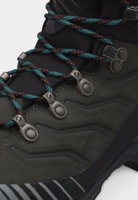 Σκούρο πράσινο ορειβατικό μποτάκι με μαύρα και μπλε κορδόνια με σχέδιο, περασμένα από μεταλλικές τρύπες, με ανάγλυφη ραφή ζιγκ-ζαγκ στην πλευρά.