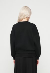 Μαύρη φόρμα με ριγ�ωτό λαιμό, υπερμεγέθεις μανίκια και ελαστική μέση. Διαθέτει απλή σχεδίαση, εμφανίζεται από πίσω.