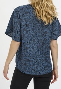 Blusa blu a fantasia con maniche corte, caratterizzata da un motivo floreale nero. Tessuto morbido con una vestibilità comoda e orlo curvo.