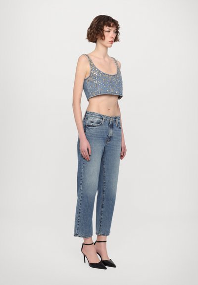 Kuttet denim topp med gullpynt, kombinert med lyseblå høytlivsjeans og svarte spisse hæler.