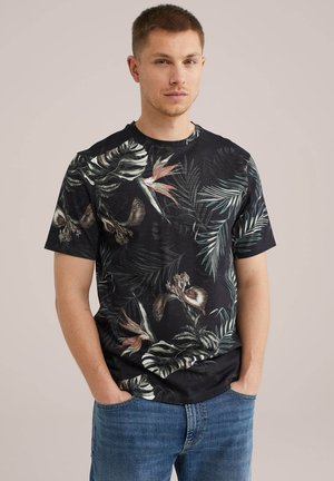 Black short-sleeve t-shirt featuring a tropical leaf and flower print in green, pink, and beige tones. Round neckline and relaxed fit.
