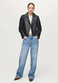 Zwarte leren motorjas met zilverkleurige hardware, gecombineerd met lichtblauwe, hoog uitgesneden wijde jeans en puntige bruine schoenen.