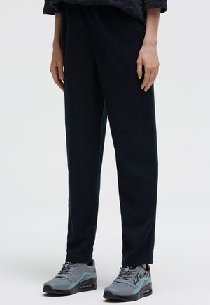 Marineblaue Cordhosen mit entspanntem Schnitt und strukturierter Textur, kombiniert mit grauen und türkisfarbenen Sneakers mit schwarzen Akzenten und einem Logo.