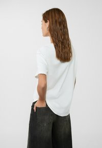 T-shirt bianco a maniche corte con vestibilità comoda, caratterizzato da un colletto rotondo e un orlo curvo, abbinato a jeans a gamba larga grigio scuro.