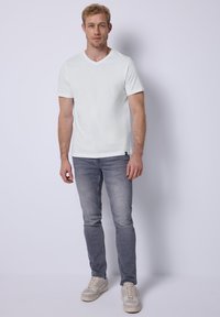 Bílý krátký rukáv V-čkový tričko spárované se světle šedými slim-fit džíny a béžovými teniskami, s jednoduchým designem a pohodlným vzhledem.