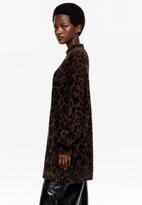 Suéter oversize de estampado de leopardo en marrón y negro, de textura suave, con mangas largas y un corte relajado, combinado con pantalones negros.