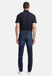 Jeans in denim scuro con una vestibilità dritta, caratterizzati da cuciture a contrasto e due tasche posteriori, abbinati a una polo navy a maniche corte.