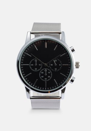 Reloj de pulsera de metal plateado con una esfera negra, tres subdiales, índices de hora plateados y una pulsera de malla plateada texturizada.