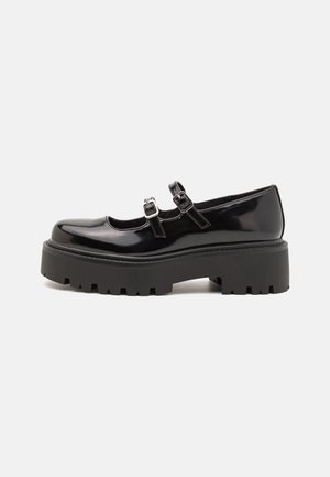 Black patent leather Mary Jane shoes with double straps, silver hardware, and a chunky, ridged platform sole. Smooth finish and rounded toe.