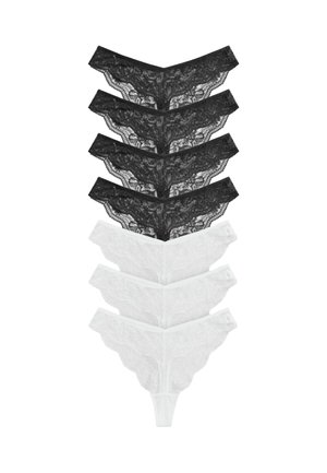 Quatre paires de strings en dentelle noire empilées au-dessus de quatre paires de strings en dentelle blanche sur un fond blanc.
