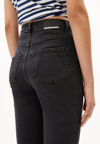 Jeans negros de tiro alto con un diseño ajustado. Presentan una etiqueta negra con "ARMEDANGELS" en la cinturilla y dos bolsillos traseros.