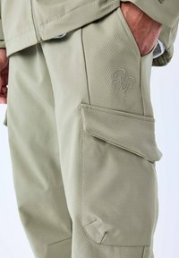 Licht olijfgroene cargobroek van textuurstof, met een voorzak en geborduurd logodetail op de dij.
