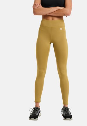 Mustard yellow high-waisted leggings with a textured pattern and logo detail. Worn with black athletic shoes featuring reflective laces.