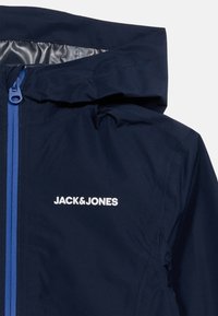 Μπλε ναυτικό μπουφάν με κουκούλα, μπλε φερμουάρ και λευκό λογότυπο "JACK&JONES" στο στήθος.