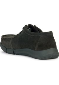 Chaussure en daim gris foncé avec un bout arrondi, des détails cousus et une semelle en caoutchouc flexible. Le design présente des accents matériels minimalistes.