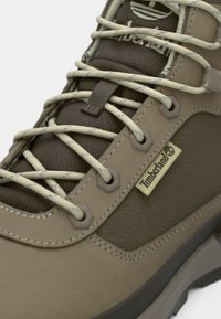 Svetlohnedá turistická obuv Timberland s béžovými šnúrkami, sieťovaným jazykom a logom na boku, ukazujúca očká a detailné šitie.