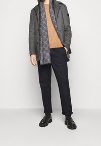 Grå uldfrakke over en tan sweater, marineblå bukser og sorte loafers. Grå tørklæde med et subtilt mønster draperet om halsen.