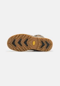 Brown hiking shoe sole with a zigzag tread pattern. Features a yellow Vibram logo, textured surface, and contrasting black accents.