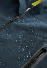 Tessuto di giacca blu scuro resistente all'acqua con motivo a rete, caratterizzato da gocce d'acqua visibili e una chiusura zip lungo il lato.