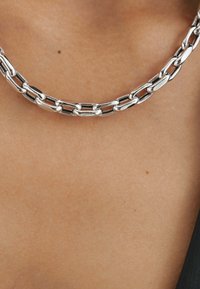 Collar de cadena de plata con segmentos ovalados y rectangulares enlazados, con una superficie lisa y pulida que descansa sobre la piel.