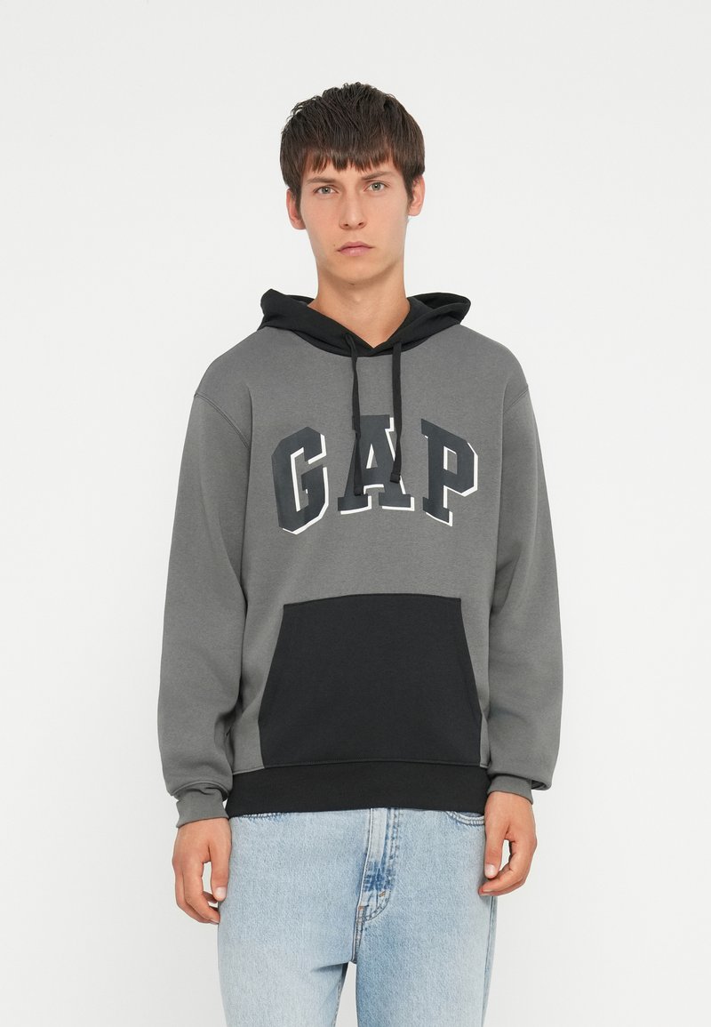 Hanorac gri cu accente negre, având logo-ul "GAP" în alb. Include o glugă și un buzunar frontal tip kangaroo, fabricat dintr-un material moale.