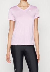 Ljusrosa v-ringad t-shirt i mjukt tyg, med korta ärmar och en vit logga på övre vänstra bröstet. Kombinerad med svarta leggings.