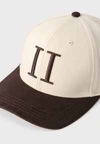 Μπεζ και σκούρο καφέ καπέλο μπέιζμπολ με κεντημένο σκούρο καφέ ρωμαϊκό αριθμό II στη μπροστινή πλευρά.